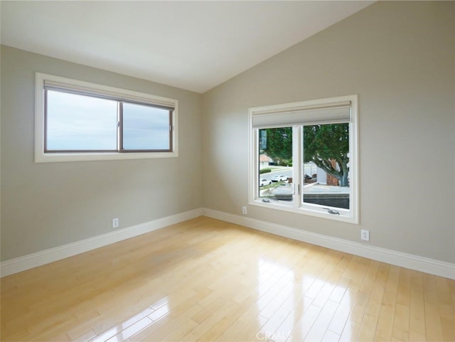 empty room with baseboards, vaulted ceiling, and light wood-style floors