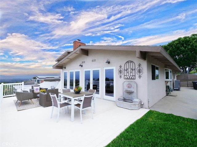 back of property with a chimney, a patio, outdoor dining space, and stucco siding
