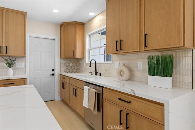 kitchen featuring light stone countertops, dishwasher, light wood-type flooring, a sink, and backsplash