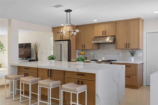 kitchen with backsplash, under cabinet range hood, visible vents, pendant lighting, and high quality fridge