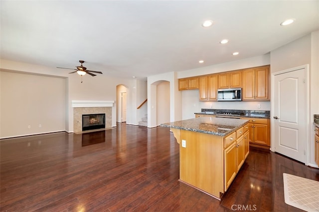 29855 Bay View Way, Menifee, CA 92584 - kitchen with a fireplace with flush hearth, dark stone counters, stainless steel microwave, ceiling fan, and a center island