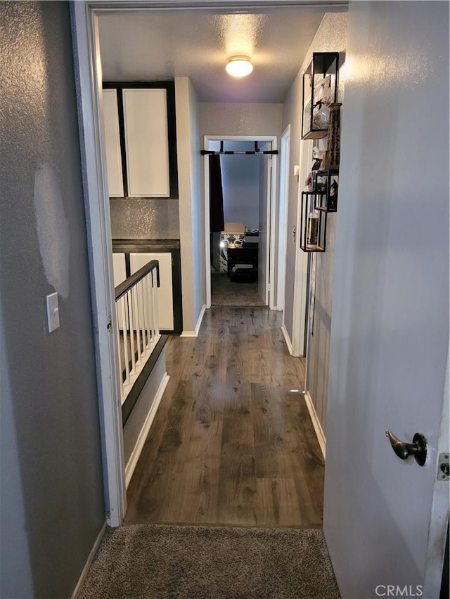 corridor featuring dark wood-type flooring and baseboards