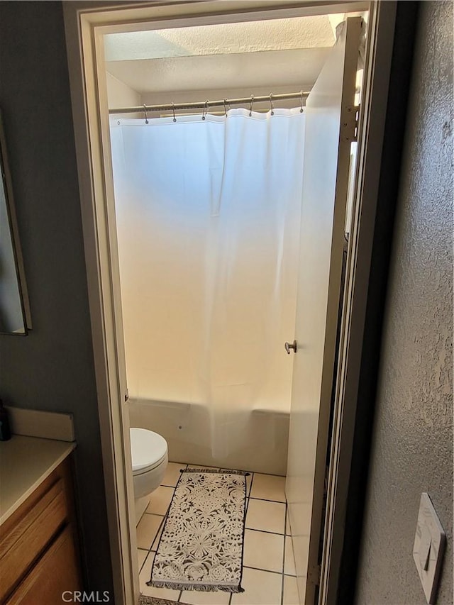 bathroom featuring shower / bathtub combination with curtain, vanity, toilet, a textured wall, and tile patterned flooring