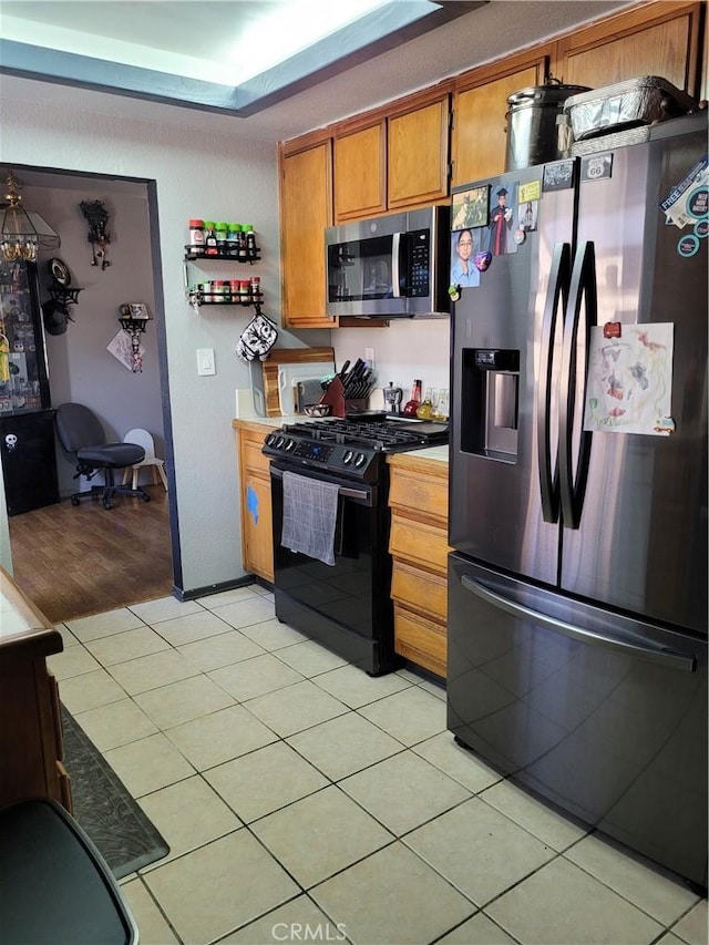 kitchen featuring light tile patterned floors, stainless steel appliances, a tray ceiling, and brown cabinets