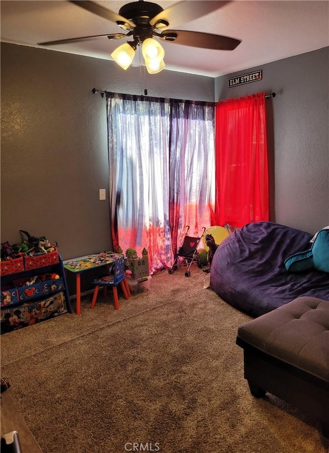 bedroom featuring a ceiling fan, a textured wall, and carpet floors