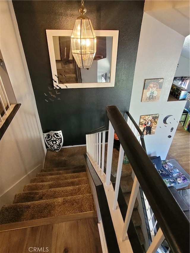 stairs with an inviting chandelier and wood finished floors
