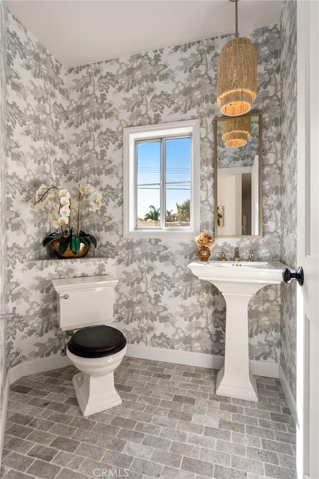 bathroom featuring baseboards, brick floor, and toilet