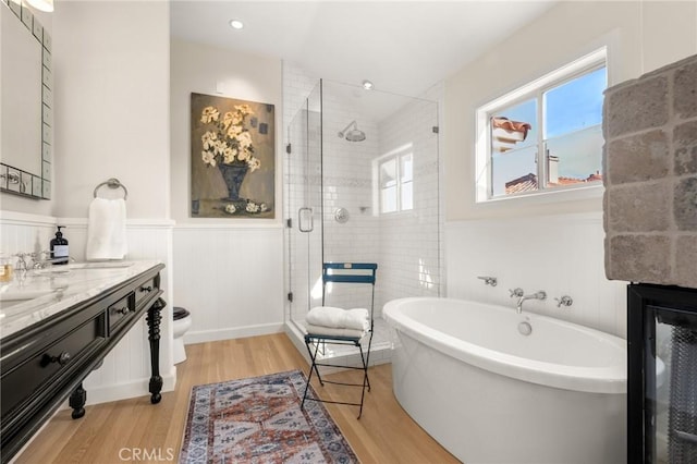 full bathroom featuring a wainscoted wall, wood finished floors, a shower stall, and a soaking tub