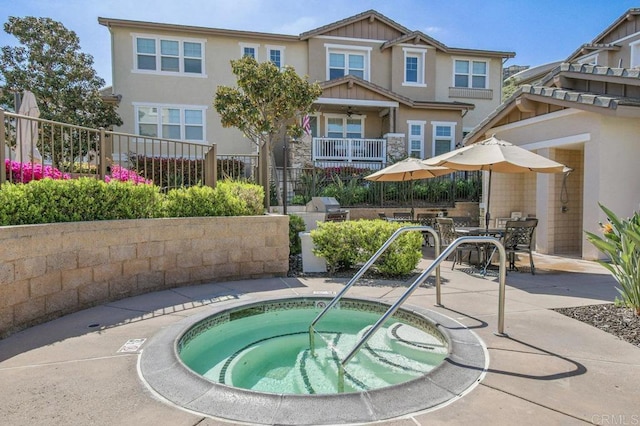 back of property featuring fence, a community hot tub, stucco siding, and stone siding