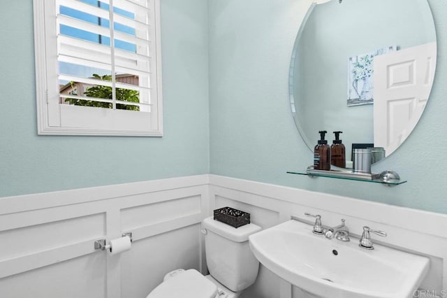 bathroom with wainscoting, toilet, a decorative wall, and a sink