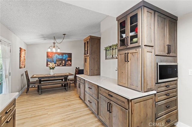 28646 Patti Ln, Menifee, CA 92585 - kitchen with light wood-style flooring, glass insert cabinets, built in microwave, decorative light fixtures, and light stone counters