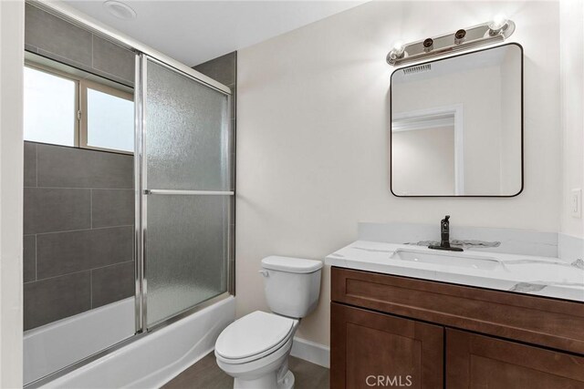 full bathroom featuring baseboards, toilet, combined bath / shower with glass door, and vanity