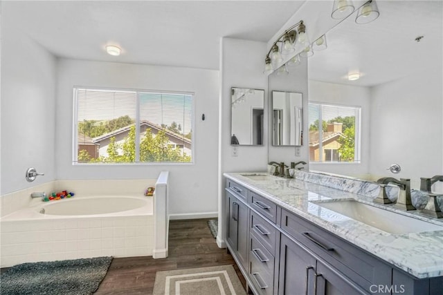 bathroom with a garden tub, double vanity, a sink, and wood finished floors