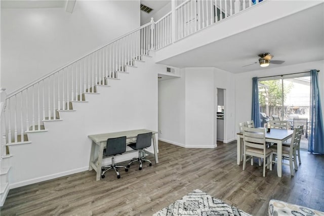 living area featuring wood finished floors, stairway, visible vents, a ceiling fan, and a towering ceiling