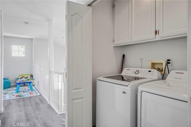 clothes washing area featuring separate washer and dryer, cabinet space, and light wood finished floors