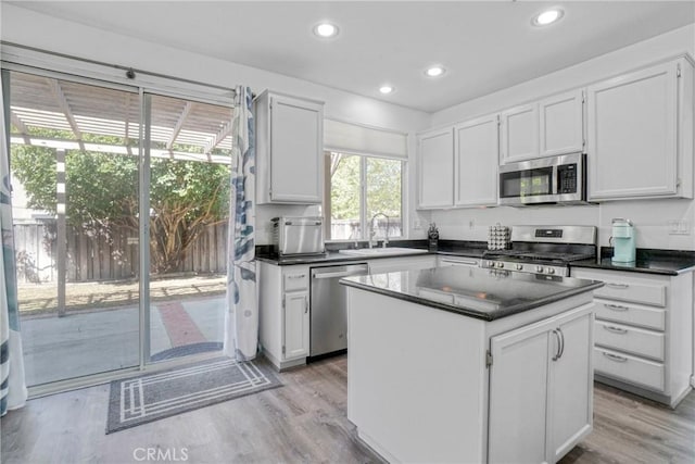 kitchen featuring appliances with stainless steel finishes, white cabinets, dark countertops, a sink, and light wood-type flooring