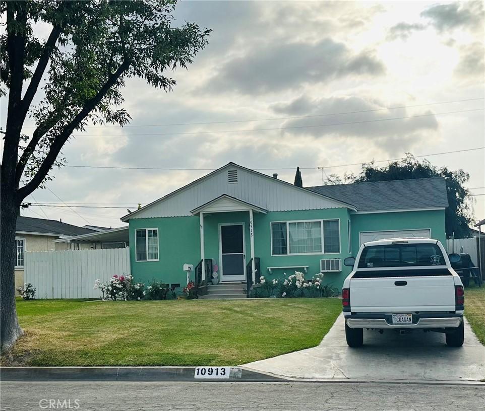 view of front facade with fence, a wall mounted AC, concrete driveway, and a front lawn