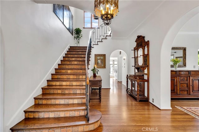 2020 N Victoria Dr, Santa Ana, CA 92706 - staircase featuring arched walkways, wood finished floors, baseboards, a high ceiling, and a chandelier