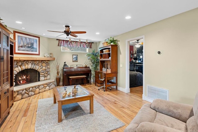 3161921 Via Puerta Del Sol, Bonsall, CA 92003 - living area with light wood-type flooring, a ceiling fan, visible vents, a stone fireplace, and baseboards
