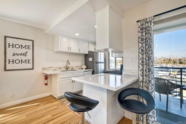 1202 N Pacific St Unit 201B, Oceanside, CA 92054 - kitchen featuring white cabinets, a sink, a breakfast bar area, light wood-style flooring, and freestanding refrigerator