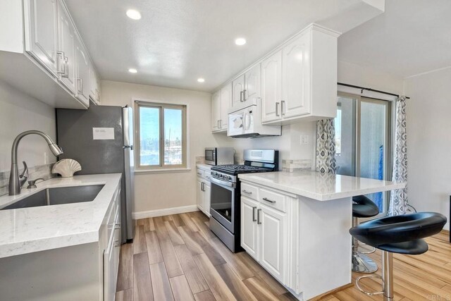 1202 N Pacific St Unit 201B, Oceanside, CA 92054 - kitchen with appliances with stainless steel finishes, a sink, white cabinetry, light wood-type flooring, and a kitchen bar