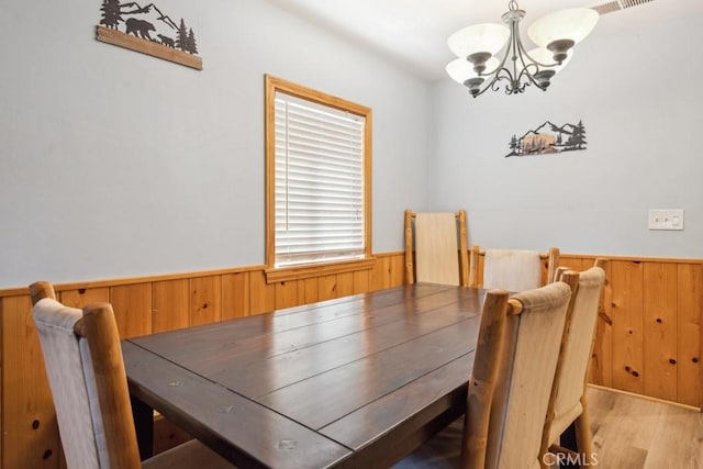 dining space featuring a wainscoted wall, a notable chandelier, wooden walls, and light wood-style flooring