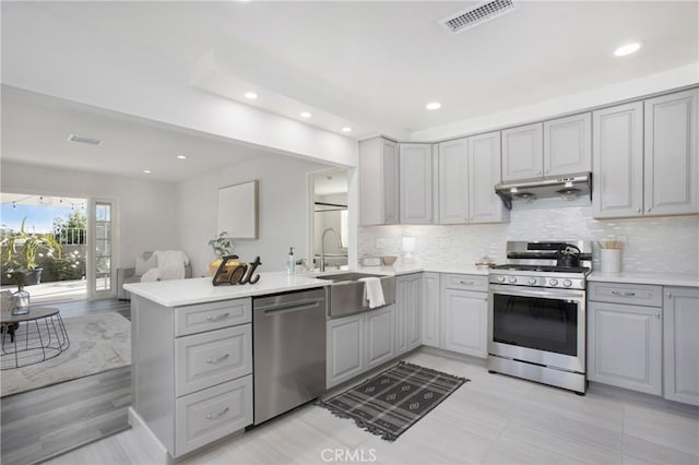 kitchen featuring stainless steel appliances, light countertops, a sink, gray cabinetry, and a peninsula