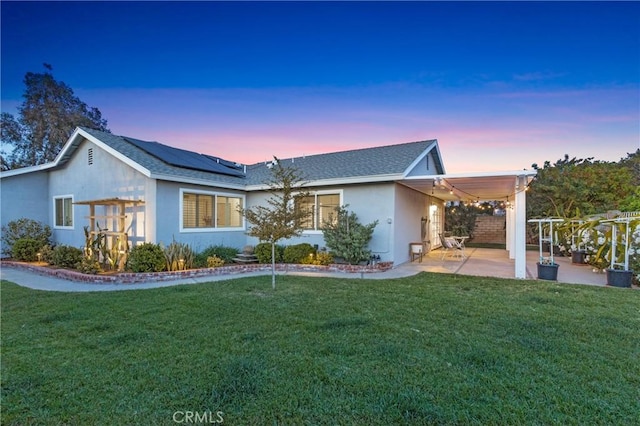 view of front of property with stucco siding, a yard, a patio, and solar panels