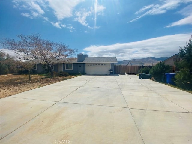 ranch-style house with a chimney, fence, concrete driveway, and an attached garage