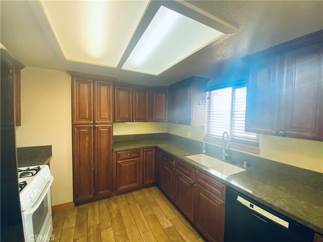 kitchen featuring white gas range oven, a sink, dark countertops, light wood-style floors, and black dishwasher