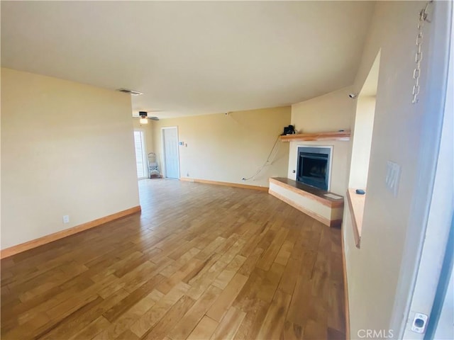 unfurnished living room with wood finished floors, ceiling fan, a fireplace with raised hearth, baseboards, and visible vents