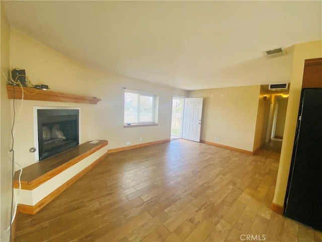 unfurnished living room with visible vents, light wood-style floors, and a fireplace with raised hearth
