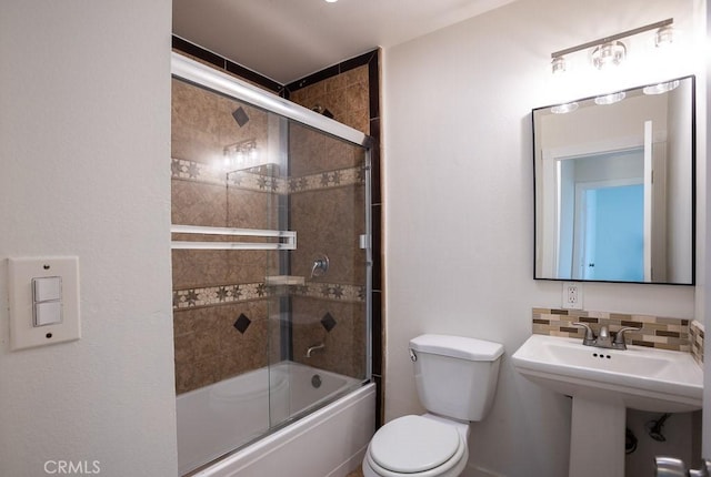 bathroom with combined bath / shower with glass door, toilet, decorative backsplash, and a sink