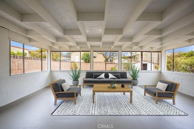 sunroom featuring finished concrete flooring, a wealth of natural light, beam ceiling, and concrete block wall