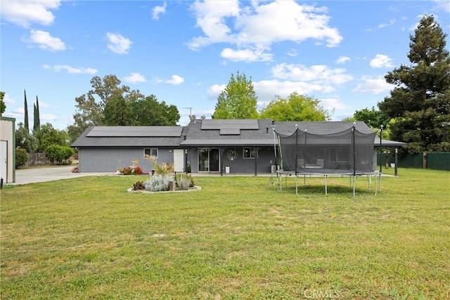 back of house featuring a lawn, fence, roof mounted solar panels, and a trampoline