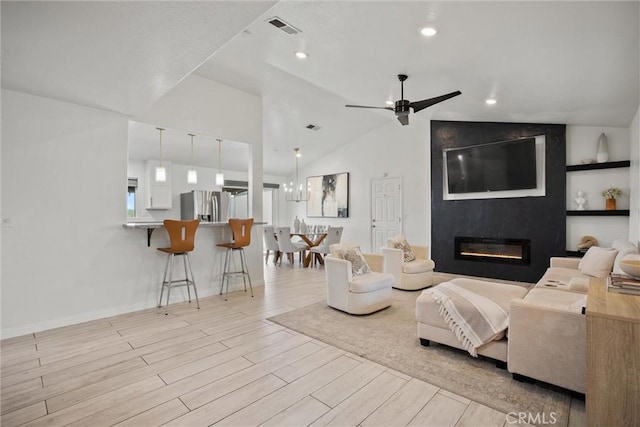 living area with visible vents, light wood-style floors, vaulted ceiling, a fireplace, and a ceiling fan