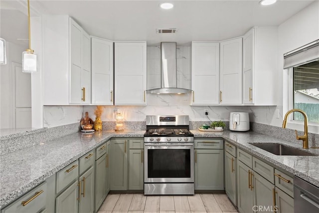 kitchen with white cabinets, wall chimney exhaust hood, appliances with stainless steel finishes, and a sink