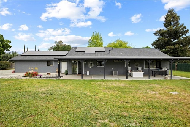 rear view of property with roof mounted solar panels, a yard, and a patio