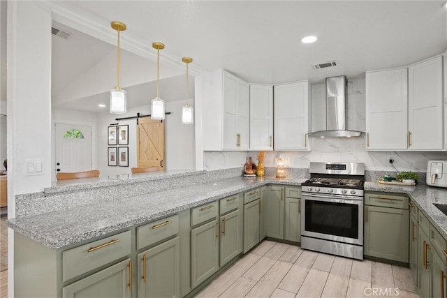 kitchen featuring a barn door, stainless steel range with gas cooktop, wall chimney exhaust hood, visible vents, and green cabinetry