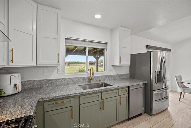 kitchen with recessed lighting, light stone countertops, a sink, stainless steel appliances, and white cabinetry