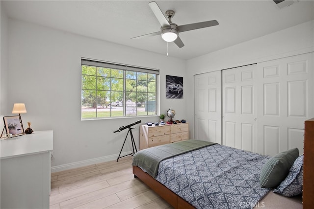 bedroom with light wood-style floors, ceiling fan, visible vents, baseboards, and a closet
