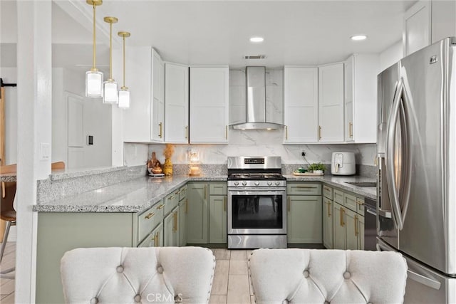 kitchen with light stone counters, green cabinetry, white cabinets, stainless steel appliances, and wall chimney exhaust hood