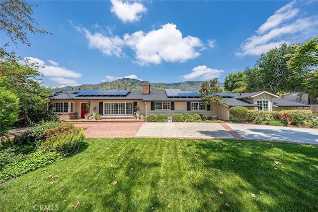 ranch-style house featuring a front lawn, roof mounted solar panels, a mountain view, and a chimney
