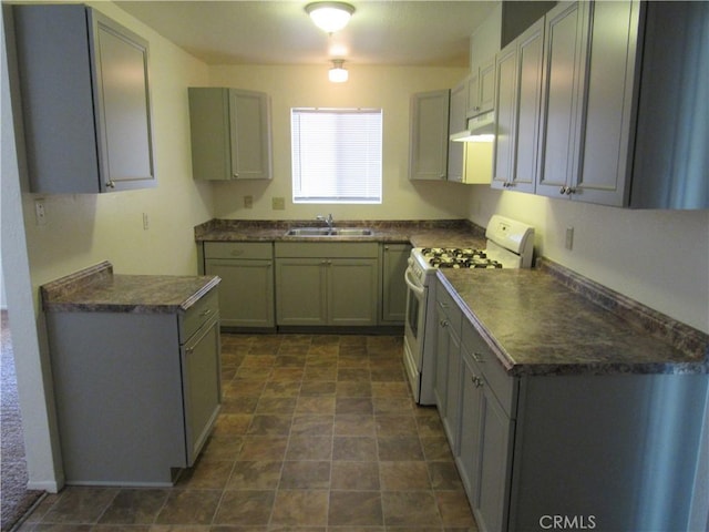 kitchen with gas range gas stove, dark countertops, under cabinet range hood, and a sink