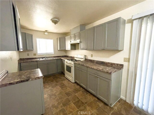 18225 Casaba Rd, Adelanto, CA 92301 - kitchen featuring gray cabinets, dark countertops, a sink, under cabinet range hood, and white range with gas stovetop