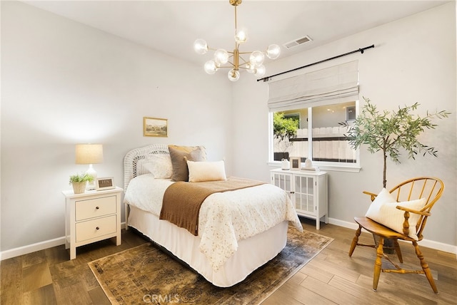 bedroom featuring an inviting chandelier, wood finished floors, visible vents, and baseboards