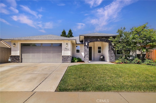 prairie-style home with stucco siding, stone siding, a front yard, concrete driveway, and an attached garage