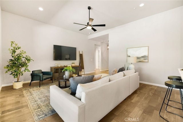 living room featuring baseboards, light wood-type flooring, a ceiling fan, and recessed lighting