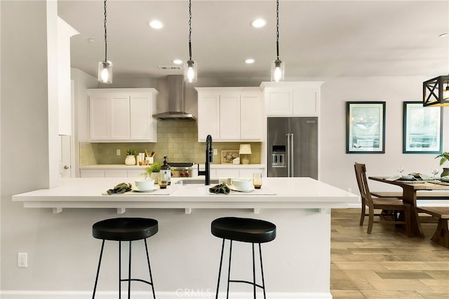 kitchen featuring wall chimney range hood, a kitchen bar, high end refrigerator, and recessed lighting