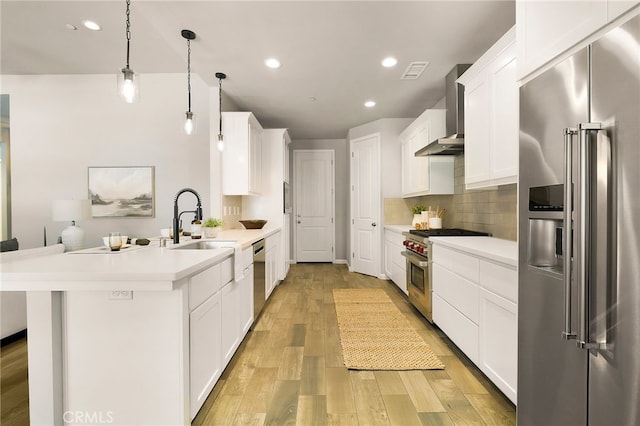 kitchen featuring high end appliances, visible vents, light wood-style flooring, a peninsula, and wall chimney range hood